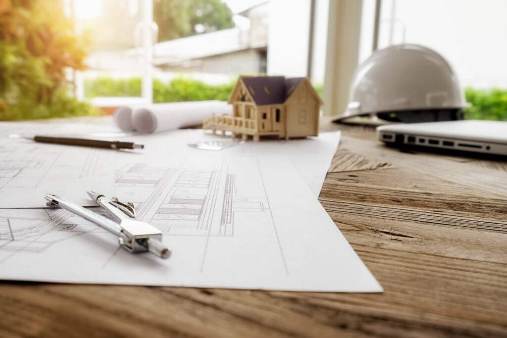 Plans architecturaux et petite maison en bois sur une table.